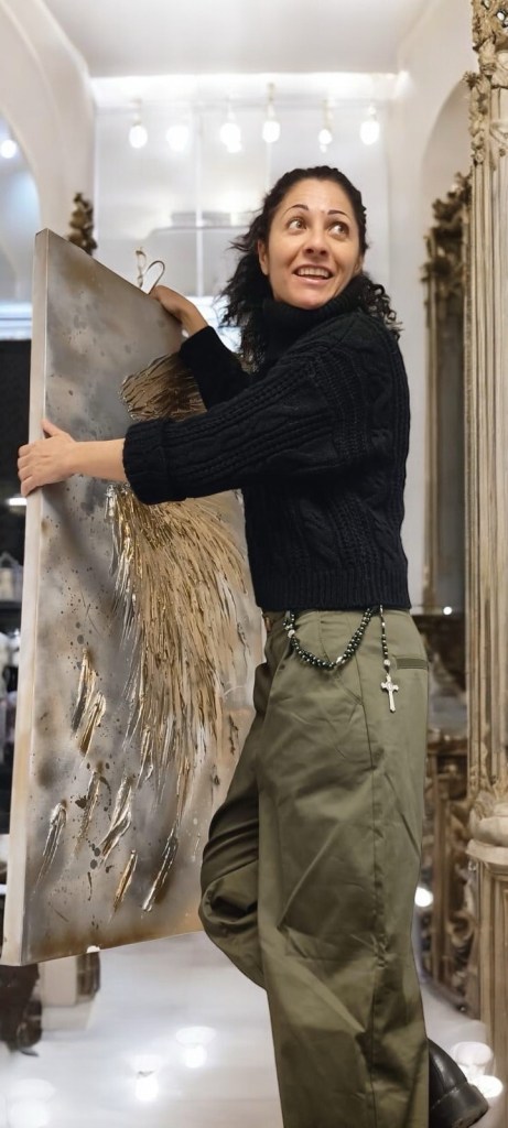 Claudia Ottone sorride mentre regge una grande tela materica con dettagli dorati, durante i preparativi per Medium Art Experience.