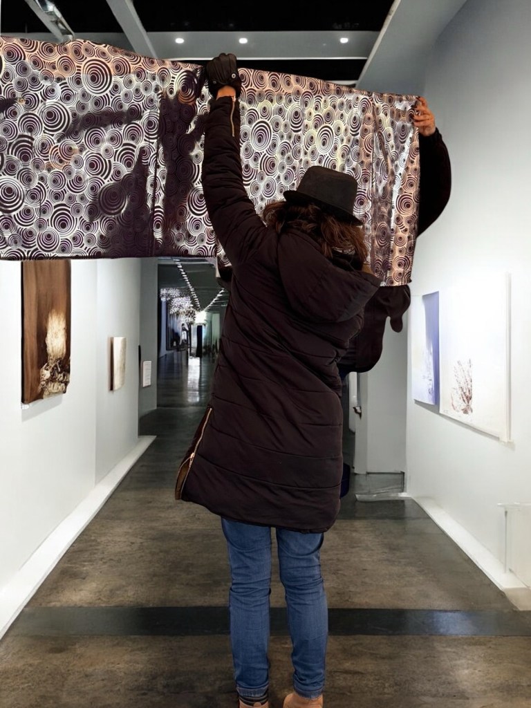 Persona di spalle solleva un grande pannello decorato con cerchi concentrici durante l’allestimento di Medium Art Experience.